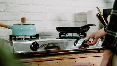 unrecognized wife in home kitchen preparing dinner for family. female hand turning on and off gas stove burner under frying pan in cooking place. woman lighting up burning stove with fire warm pot